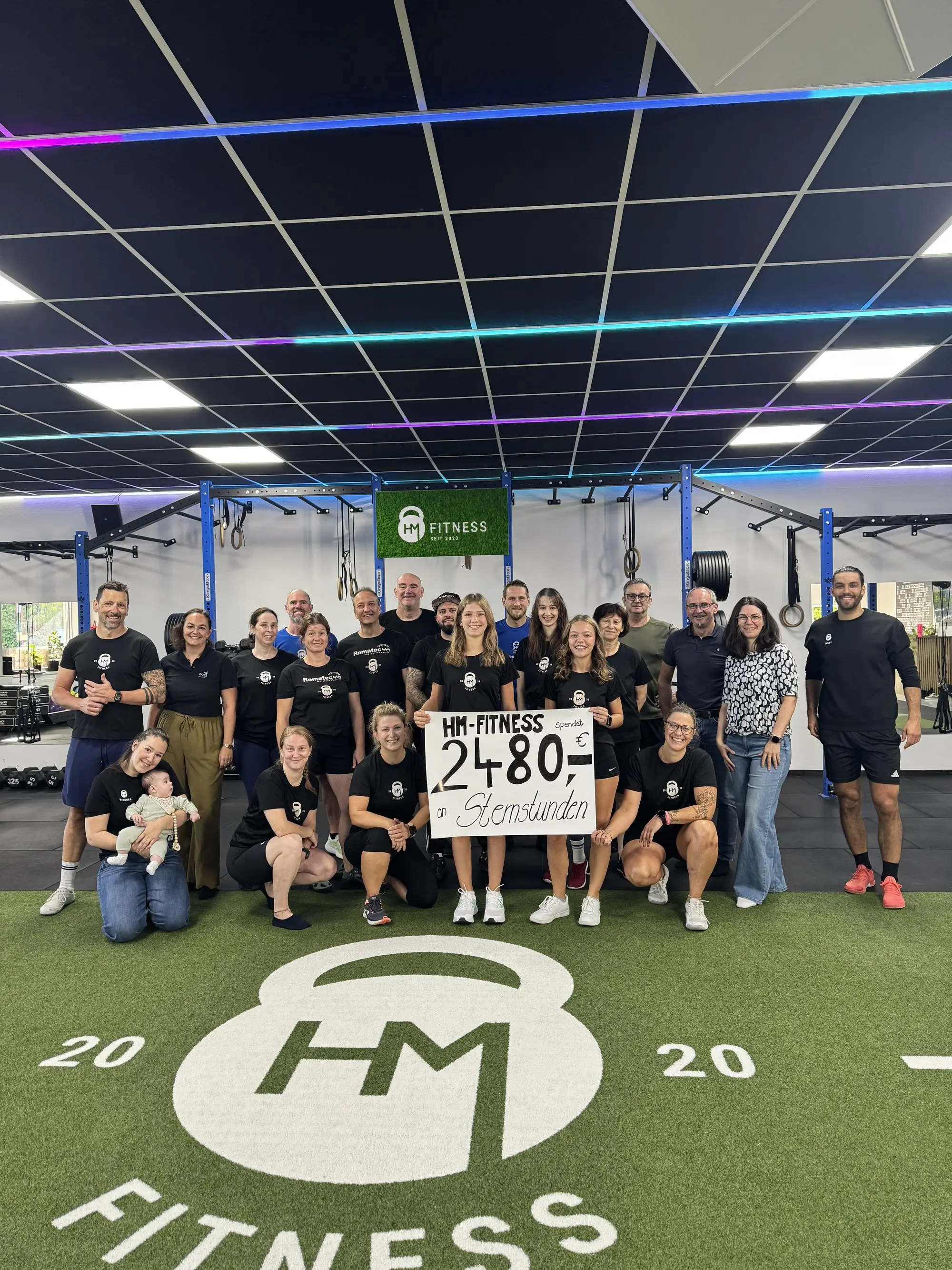 Die HM-Fitness-Community mit dem Schild 2.480 Euro für Sternstunden e.V. auf dem Studio-Bodenlogo