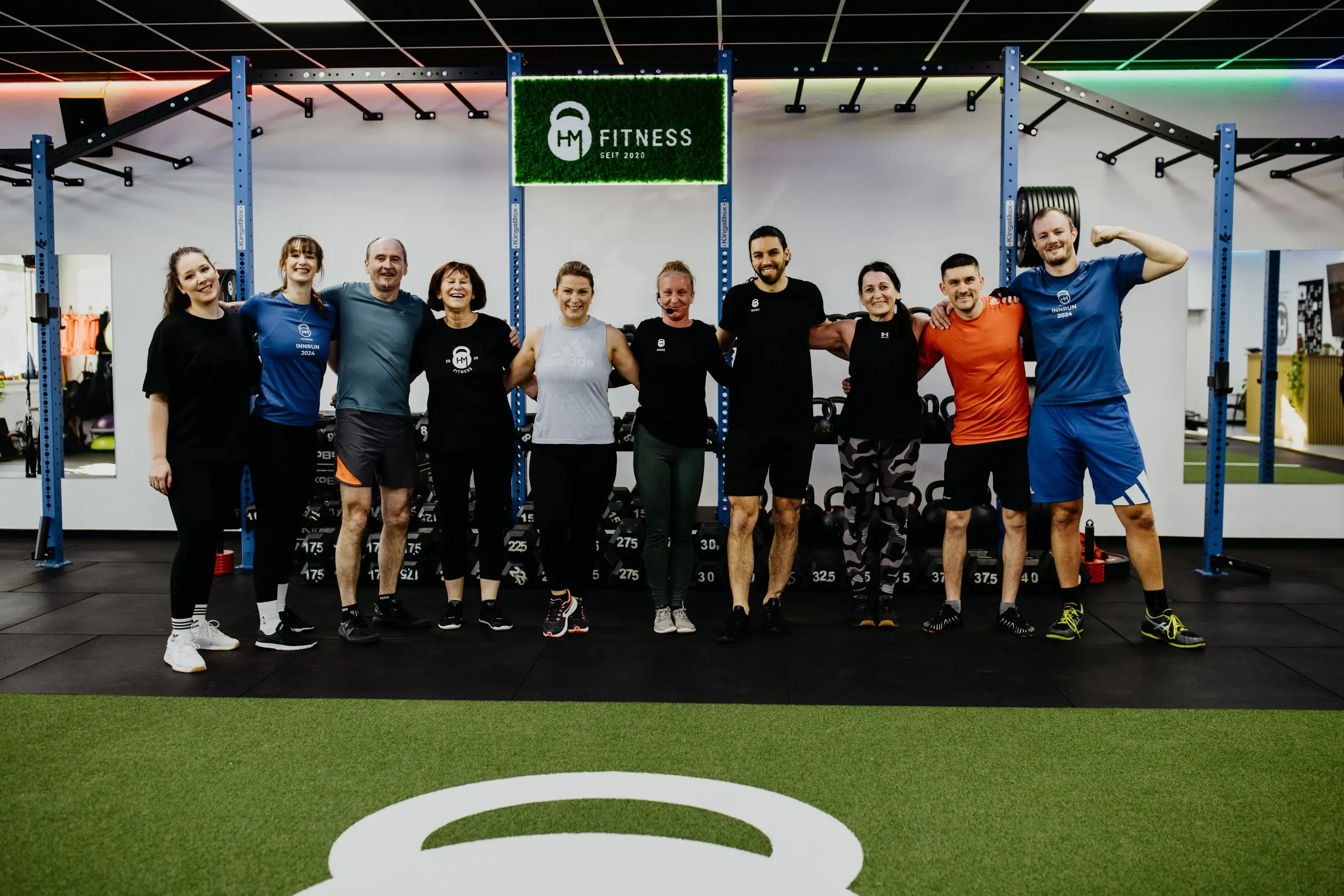 Eine Trainingsgruppe steht gemeinsam vor dem HM-Fitness-Schild